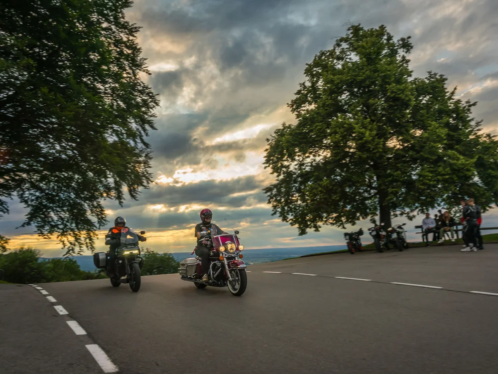 Two motorcyclists riding past a curve at sunset.