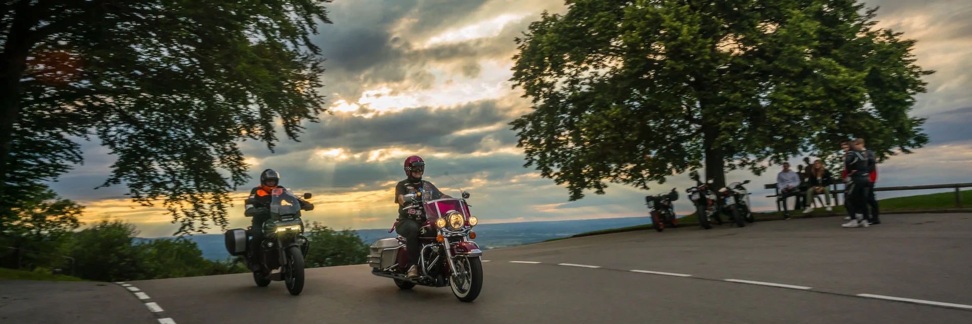 Twee motorrijders rijden bij zonsondergang een bocht voorbij.