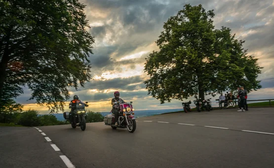 Zwei Motorradfahrer fahren bei Sonnenuntergang an einer Kurve vorbei.