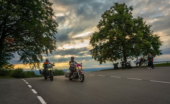 Motorradurlaub in der Region Rosenheim - Oberbayern © Moppetfoto.de Zwei Motorradfahrer fahren bei Sonnenuntergang an einer Kurve vorbei.