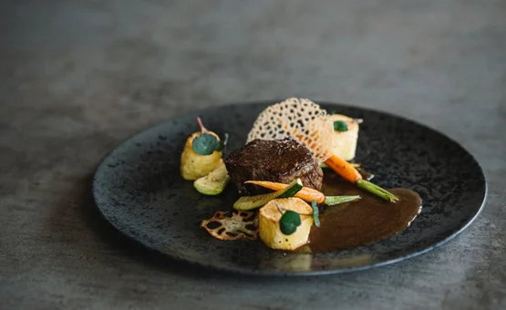 Gourmetgericht mit Steak, Gemüse und Soße auf schwarzem Teller