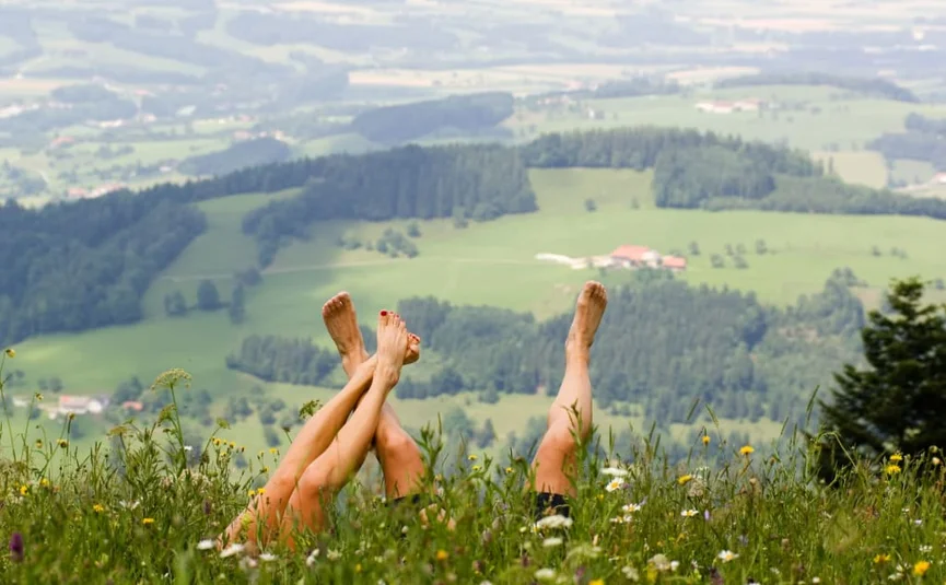 Zwei Paare liegen auf Wiese mit erhobenen Beinen und Blick auf Berglandschaft