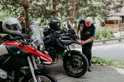 Stoderzinken Tour Mann überprüft Motorrad im Freien neben Bäumen und Helmen