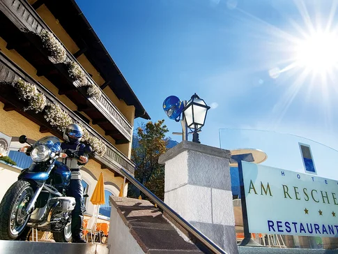 Motorradfahrer vor Hotel Am Reschensee an sonnigem Tag