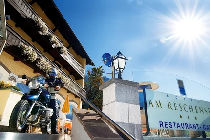 Motorradfahrer vor Hotel Am Reschensee an sonnigem Tag
