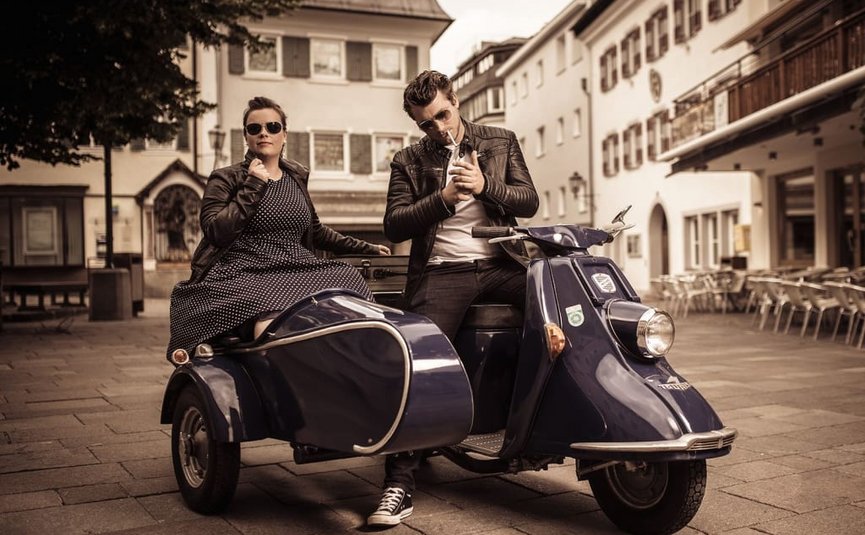 Couple in leather jackets on a blue vintage motorcycle with sidecar in town