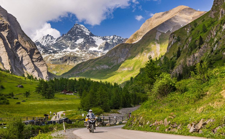 Erlebnishotel Kärnten-Mölltal ***S © Alexander Seger Motorradfahrer auf Bergstraße mit schneebedeckten Alpen und grüner Landschaft