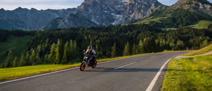 Motorradfahrer auf Bergstraße mit Bergen und Wald im Hintergrund