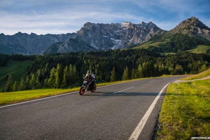 Motorradfahrer auf Bergstraße mit Bergen und Wald im Hintergrund