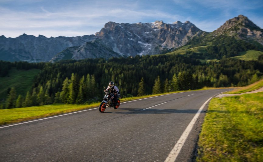 Motorradfahrer auf Bergstraße mit Bergen und Wald im Hintergrund