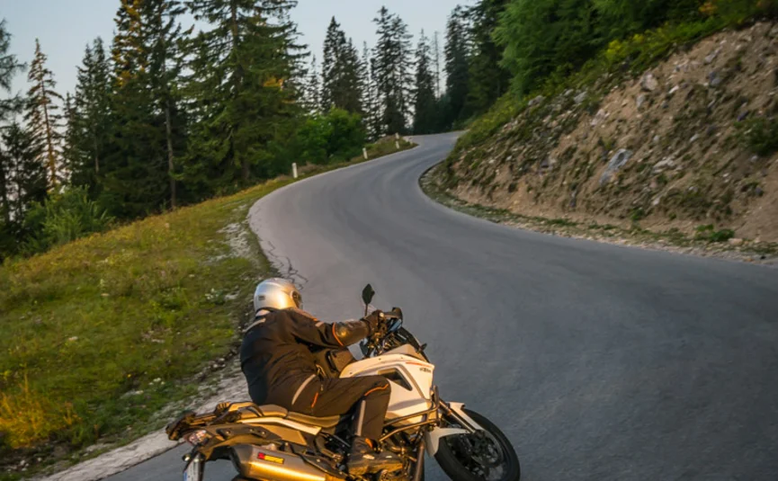 Motorcyclist riding a curve on mountain road at sunset