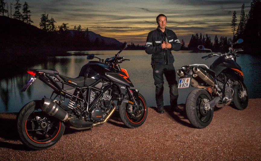 Motorradfahrer steht zwischen zwei Motorrädern am See bei Sonnenuntergang