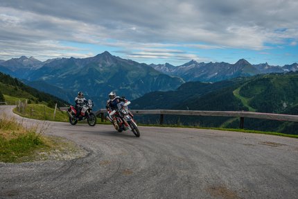 Zwei Motorradfahrer fahren auf Bergstraße mit Alpen im Hintergrund