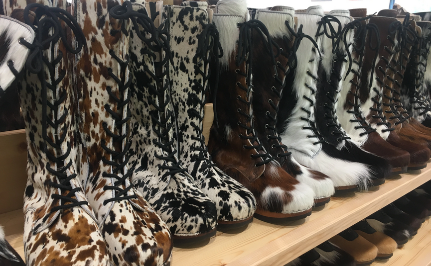 Reihe von bunten, gefleckten Fellstiefeln mit Schnürung auf einem Holzregal
