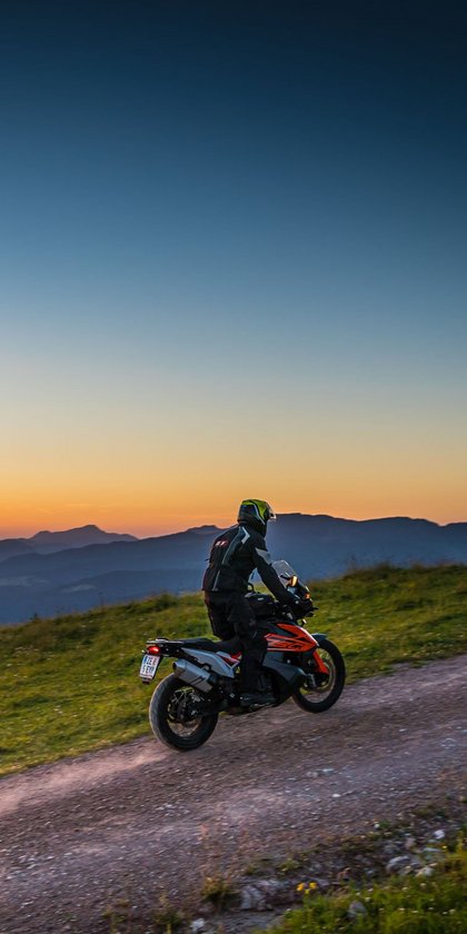 Motorradfahrer auf Bergweg bei Sonnenuntergang mit Alpenpanorama
