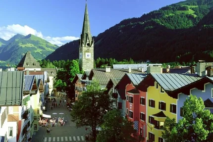 Colorful street with church tower and forested mountains on a sunny day