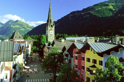 Kitzbüheler Hansi Tour (Gerlos - Zillertal - Kitzbühel) Bunte Häuserstraße und Kirchturm vor bewaldeten Bergen bei Sonnenschein