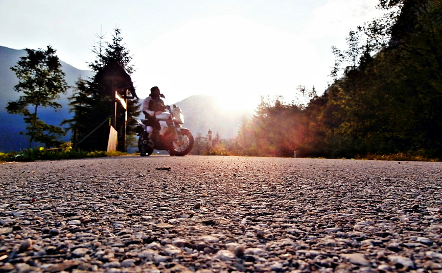 Motorradfahrer auf Landstraße bei Sonnenuntergang in den Bergen