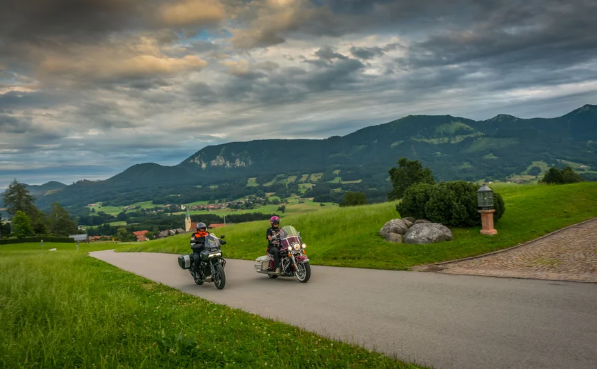 Gasthof Hotel Zur Post Samerberg *** © Moppetfoto.de Zwei Motorradfahrer fahren auf einer Straße durch eine grüne Berglandschaft