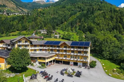 Erlebnishotel Kärnten-Mölltal © Erlebnishotel Kärnten Mölltal Alpine hotel with solar panels and motorcycles against a forested mountain backdrop