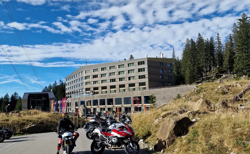 Motorcycles parked by a large hotel in alpine landscape on a sunny day