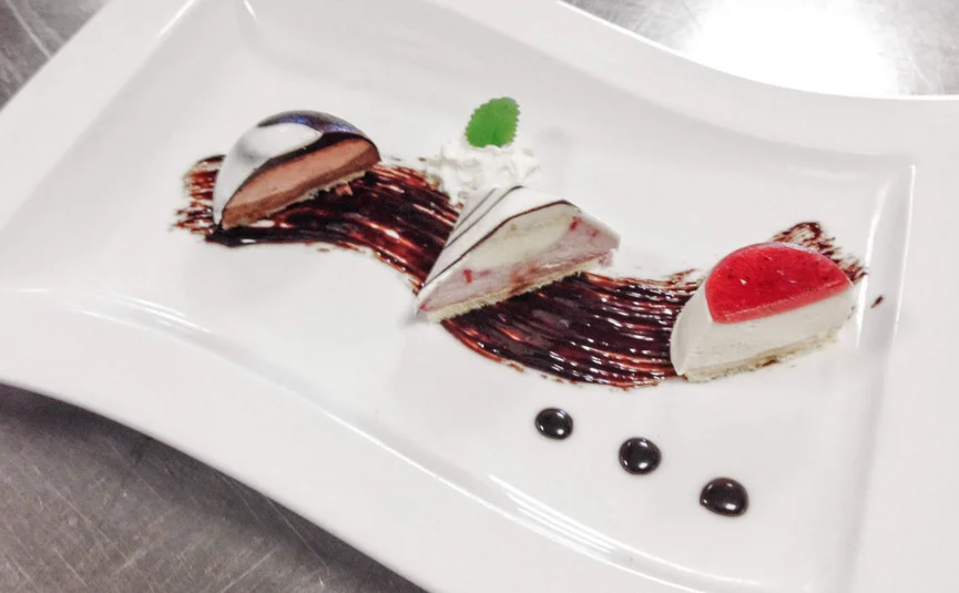 Three small dessert pieces artfully arranged on a white plate with chocolate sauce