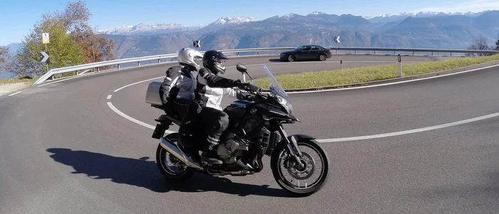 Two motorcyclists on winding mountain road with mountains in the background