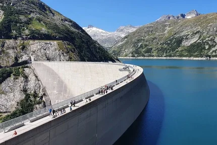 People walking on a large dam surrounded by mountains