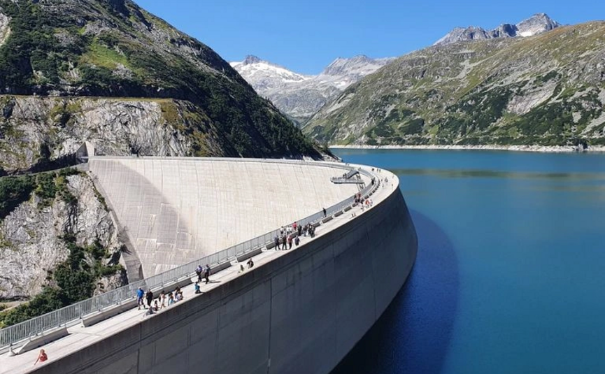 Menschen spazieren auf einem großen Staudamm in den Bergen