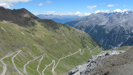 Serpentinenstraße in den Alpen bei klarem Himmel und Bergen im Hintergrund