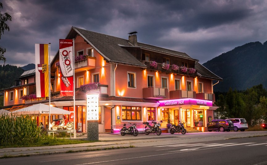 Beleuchtetes Hotel mit Motorrädern und Autos bei Abenddämmerung