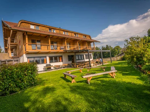 Holzhaus mit Terrasse und Sitzbänken auf grünem Rasen unter blauem Himmel
