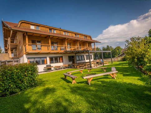 Houten huis met terras en bankjes op groen gras onder blauwe lucht