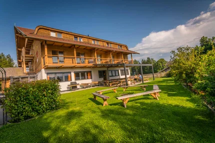 Holzhaus mit Terrasse und Sitzbänken auf grünem Rasen unter blauem Himmel