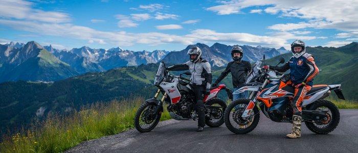 Drei Motorradfahrer mit Helmen auf Bergstraße vor Alpenkulisse