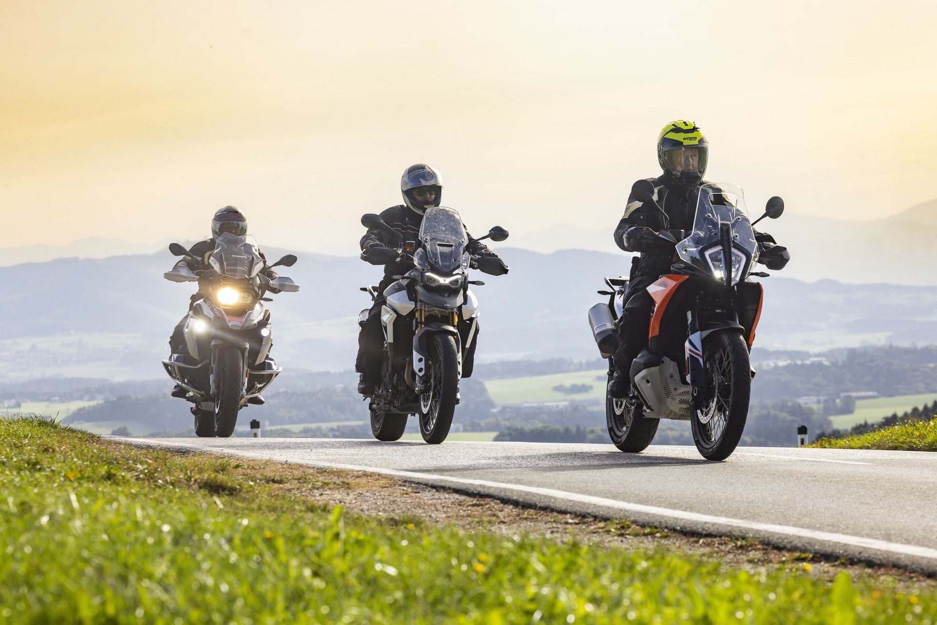 Drei Motorradfahrer fahren auf einer Landstraße mit Hügeln im Hintergrund