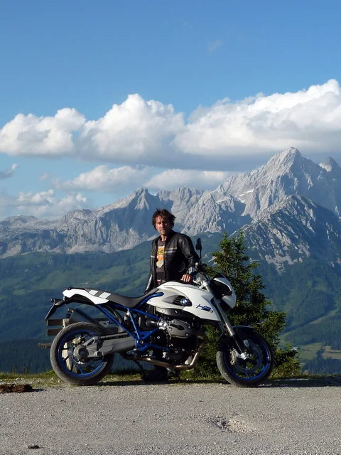 Man with motorcycle in front of mountain landscape and blue sky