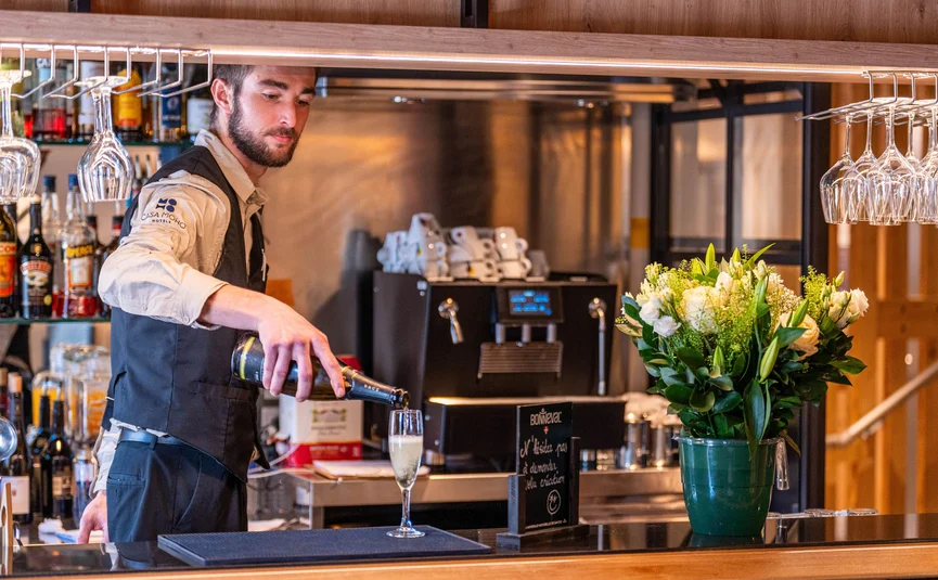 CASA MOHO Saint-François-Longchamp ***S © Jeremi MARIE Photography Barman schenkt champagne in een glas bij een bar met bloemen en glazen