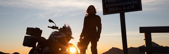 Person with motorcycle at sunset next to sign switchback 6 Edelweissleite