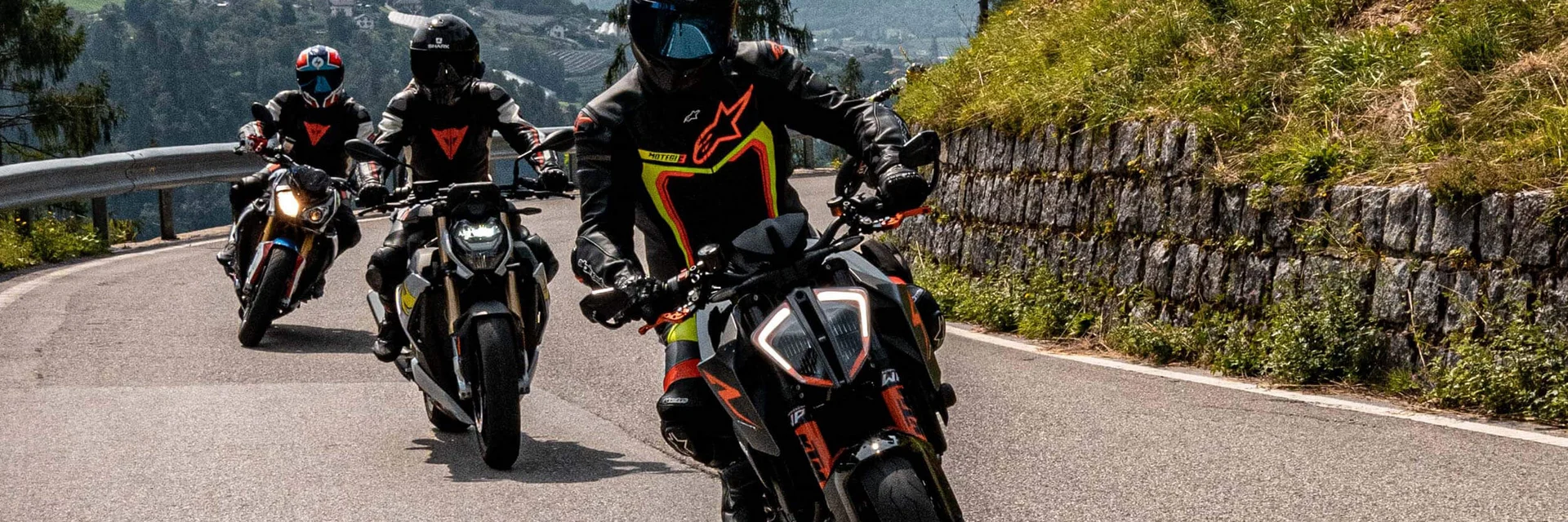 Three motorcycles riding on a mountain road with riders in protective gear