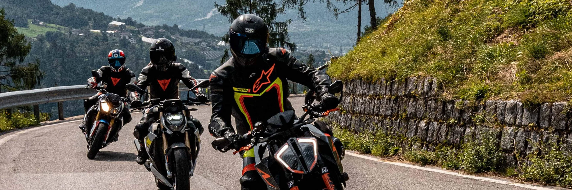 Val di Fiemme © Andrea Acler Drei Motorräder fahren auf einer bergigen Straße mit Fahrern in Schutzkleidung