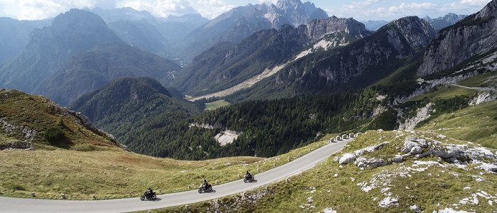 Drie motorfietsen rijden een kronkelende bergweg in de Alpen