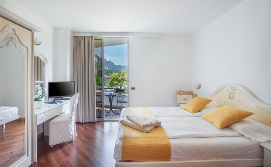 Bright hotel room with two beds, TV, and balcony with mountain view