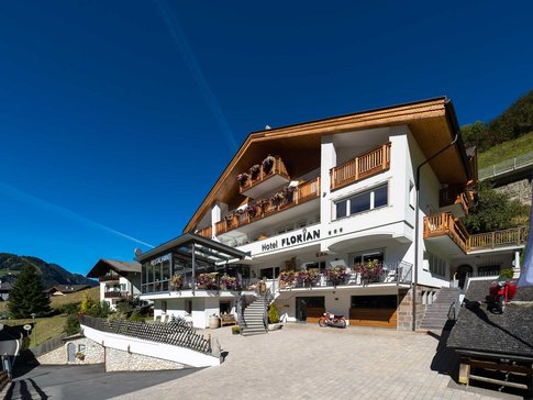 Hotel Florian mit Holzbalustraden und Blumen unter klarem blauem Himmel