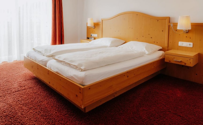 Hell eingerichtetes Schlafzimmer mit Doppelbett und roten Teppichboden