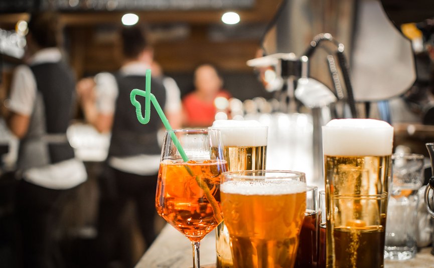 Getränke mit Bier und Cocktail auf der Bar mit unscharfen Kellnern im Hintergrund