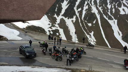 Motorradfahrer und Auto an einem Bergpass mit Schnee auf den Bergen
