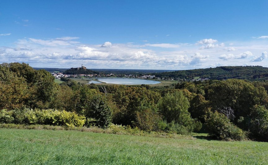 Blick auf eine grüne Landschaft mit einem See und einer Burg im Hintergrund