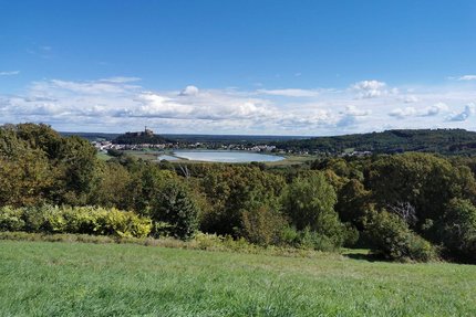 Blick auf eine grüne Landschaft mit einem See und einer Burg im Hintergrund