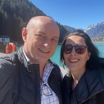 Motorradurlaub in Kärnten © Hotel Gasthof Strasswirt Lächelndes Paar vor Bergsee und schneebedeckten Bergen bei klarem Himmel